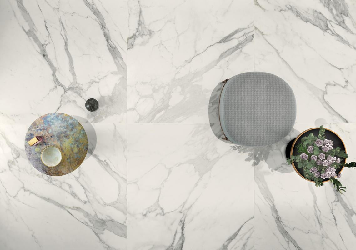 Three decorative items on a marble look tile surface: a round metallic object, a gray textured sphere, and a circular