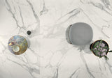 Three decorative items on a marble look tile surface: a round metallic object, a gray textured sphere, and a circular